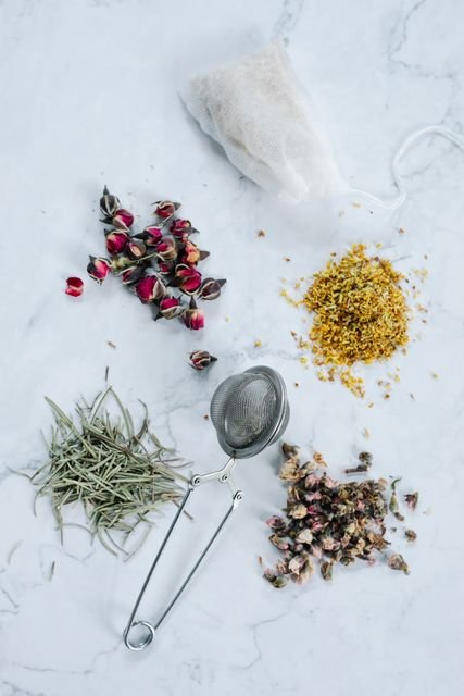 Assorted dried herbs and flowers arranged around a tea infuser