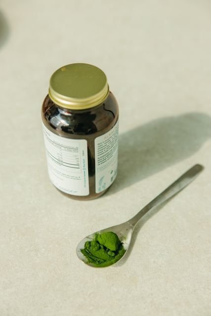 Zena Greens Review: Ingredients, Evidence, Safety, and Is It Worth It? 2 Green supplement powder on a spoon beside a supplement jar