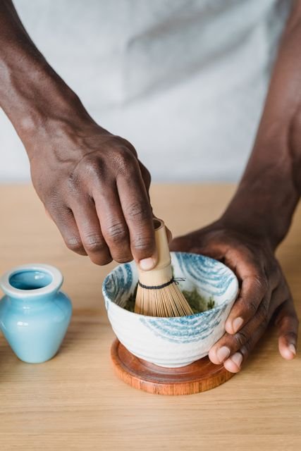 Hands whisking green matcha in a ceramic bowl