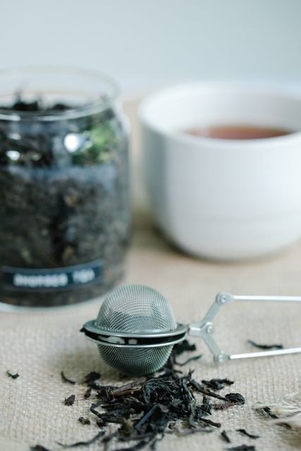 Loose leaf tea beside a metal tea infuser and cup
