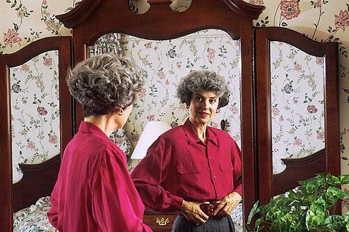 Older woman looking at her reflection in a bedroom mirror