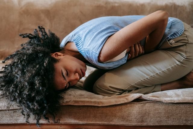 Woman curled up on a couch holding her stomach