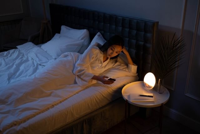 Woman lying in a dim bedroom while looking at her phone