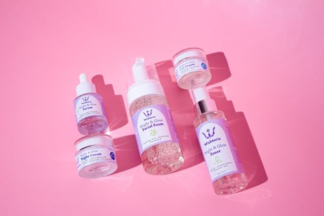 Assorted skincare bottles and containers arranged on a pink surface