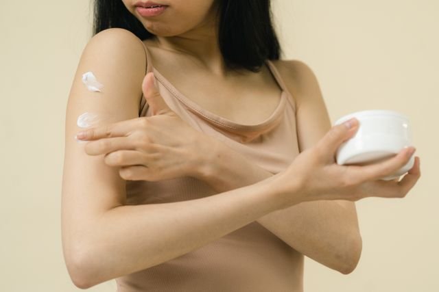 Woman applying moisturizing cream to her upper arm