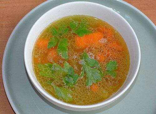 Bowl of golden bone broth with carrots and parsley