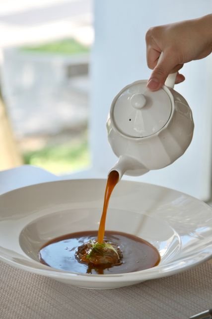 Broth being poured from a white pot into a bowl