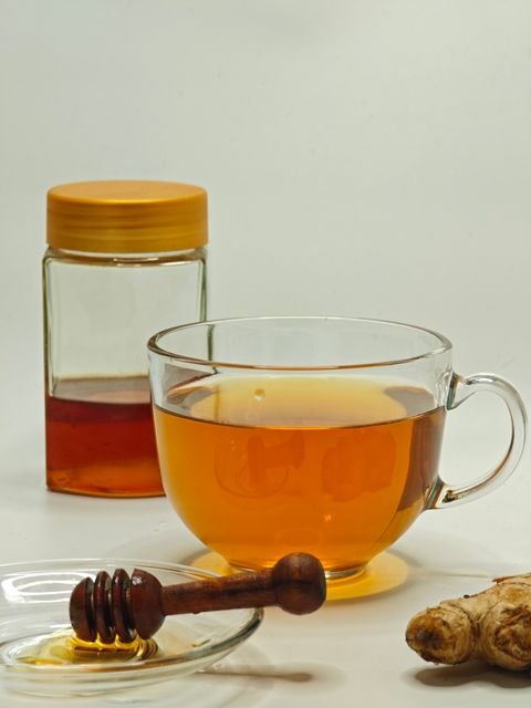 Glass cup of ginger tea beside fresh ginger and honey