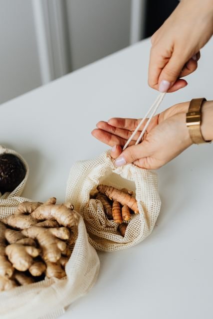 Hands holding fresh ginger and turmeric in drawstring produce bags