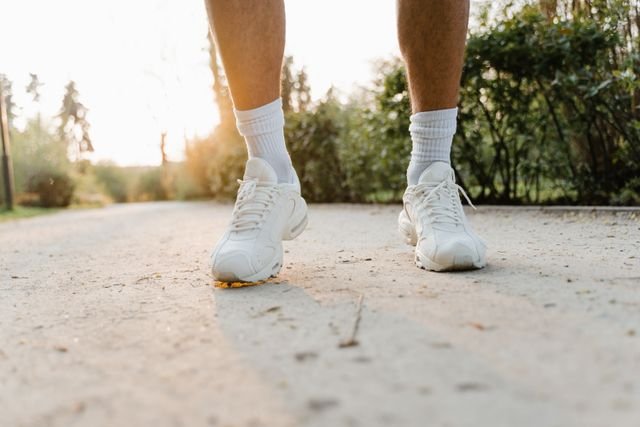 Person wearing white sneakers walking along a sunlit path