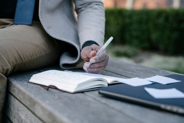 Person writing notes in an open notebook outdoors