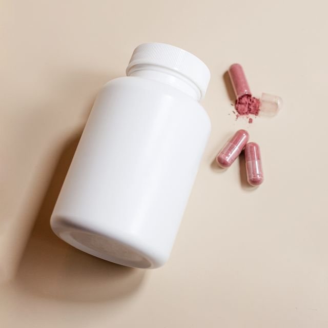 Unlabeled white supplement bottle beside pink capsules