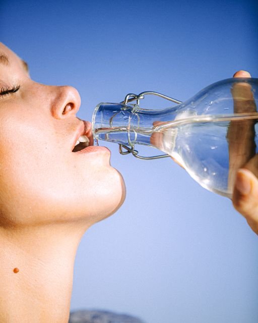 Woman drinking water from a clear glass bottle outdoors