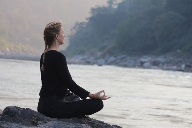 Woman meditating beside a river in the morning