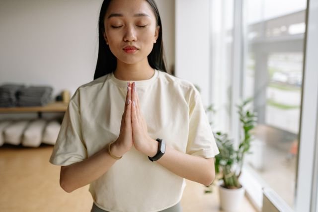 Woman sitting indoors with eyes closed and hands together