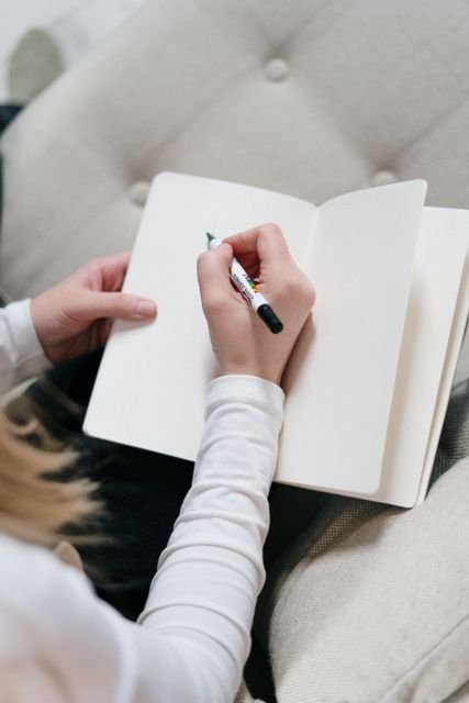 Person writing in an open notebook while seated in a chair